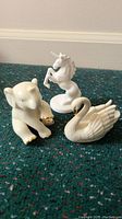 Three porcelain figurines shown together: baby elephant with gold accents, unicorn, and swan.
