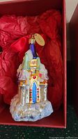 Close-up photo of the glass castle ornament showing colorful details, snow base, and attached Lenox tag in red cushioned box.