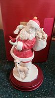 Front view of hand painted Santa Claus figurine with deer standing at base and cardinal perched on arm and sack.