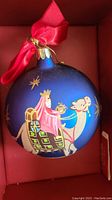 Close-up of Lenox blue glass ornament depicting one of the Three Wise Men riding a camel, decorated with stars and a red fabric bow on top.