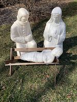 Photo showing all three white molded plastic lighted nativity lawn figures: Mary and Joseph standing or kneeling, and Baby Jesus lying in a wooden manger on grass.
