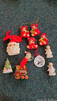 Full set of 11 vintage Christmas ornaments and decor items arranged on carpet: 4 red ceramic bear band ornaments, cloth red bear band ornament, Santa face ornament, Christmas tree figure, angel figurines, train ornament, round ornament with winter scene.