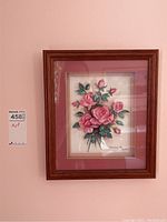 Framed artwork showing pink roses with 3D effect in wooden frame with pink matte and white background. Signed by Mildred Reeve.