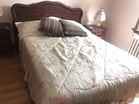 Bed with floral bedding, pillows, striped cushions and wooden headboard