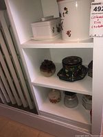Three shelves with various ceramic kitchen decor including canisters, teapot, small floral decorated tins, and containers