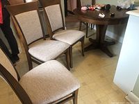 Four Canadel wood dining chairs with light beige upholstered seats and backs assembled together.