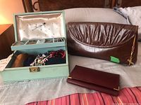 Photo showing light blue jewelry box open to reveal costume jewelry, brown leather clutch resting behind, and brown wallet in front