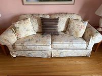 Front view of floral upholstered couch with two floral cushions and one striped cushion, showing overall condition and design.