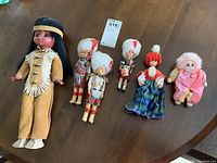 Full group shot of all six dolls displayed on a wooden table, showing size and costume details