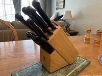 Front angle view of the wooden knife block stand holding knives with black handles showing brand logo and handle shapes.