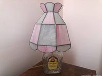 Lamp with stained glass shade in pink and white and a Crown Royal whiskey bottle base on a wooden table.