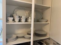 Full view of china set inside cabinet including stacked plates, bowls, tea cups, and saucers.