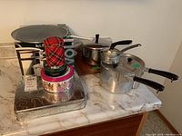 Four metal pots with black handles including a pressure cooker on a countertop with four decorative round tins stacked nearby