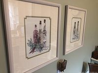 Two framed prints hung on a wall featuring bottles and botanical elements, signed Hamboo.