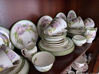 Photo showing Royal Doulton porcelain plates, cups, saucers, creamer, and sugar bowl neatly arranged on a cabinet shelf.