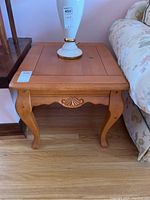 Front view of the wood side table showing carved apron and curved legs with a lamp on top (lamp not included).