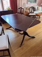 Photo showing a dark wood dining table with two pedestal bases, extended on one side with the leaf piece attached.