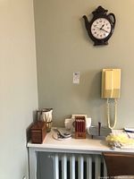 Wide shot showing the items on a white tabletop and the teapot clock mounted on the wall above, capturing the overall lot.
