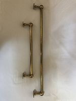 Two brass towel bars of different lengths with brass decorative ends and wall mounts, laid flat on a white background.