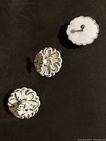 Photo of three cream-colored metal drawer knobs with gold embossed floral designs, showing front and back, includes screws.