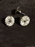 Three cream colored metal drawer knobs with gold leaf embossing shown on dark fabric.