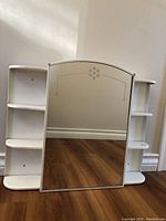 Front view of white metal bathroom cupboard with a large mirror and open shelves on both sides.