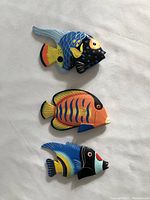 Top down view of 3 colorful wooden fish ornaments laid on a white surface showing their shape and paint detail.