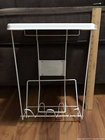 White metal garbage holder for cupboard door with pop-up lid closed. A wooden ruler is placed beside it for size reference.
