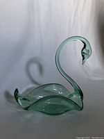 Green glass swan shaped dish photographed against white backdrop showing curved neck and body that forms a shallow dish