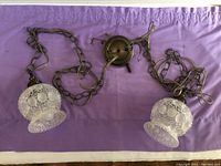 Full view of the two hanging lamps connected by chains with glass shades, laid flat on purple fabric.