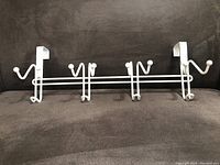Front view of white metal over the door hanger showing four dual hooks with bottom hooked hangers.