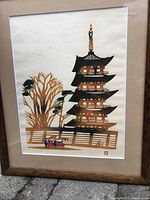 Front view of framed watercolor art depicting a traditional Japanese shrine with multiple tiers and trees, featuring a red artist stamp.