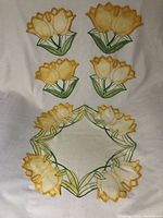 Full set of embroidered yellow tulip placemats and circular wreath mat laid out on white background.