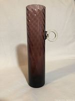 Full view of the tall purple glass vase showing the swirl texture and loop handle on plain background.