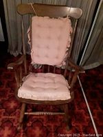 Front view of wooden rocking chair with pink tufted cushions on seat and backrest.