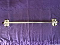 Top side view of full towel bar showing cream finish and gold embossed mounts lying flat on purple fabric surface.