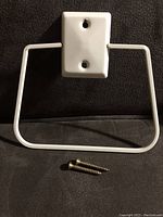 Front view of the cream color metal towel holder with two mounting screws in front on a black surface.