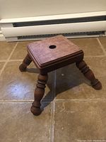 Front view showing square top with central hole and turned legs on tiled floor.