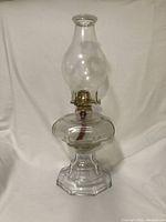Clear glass 1950s hurricane lamp with hexagonal base and brass wick burner beneath glass chimney.