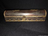 View of front of rectangular wooden box closed, showing metal clasp and decorative scalloped edging.