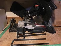 Side view of the Craftsman 10-inch compound miter saw on a wooden surface with dust collection bag visible.