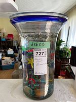 Full view of glass vase with label showing measurements and item description, visible water and shapes beneath surface.