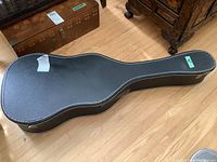Closed black hard-sided guitar case with white binding and metal latches on wood floor