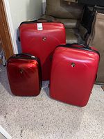 Full view of three red Heys hard case luggage pieces standing next to each other showing size differences and condition.