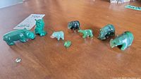Overview of all eight jade and malachite animal figurines arranged on a wooden surface showing size range and color details.