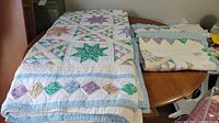 Full view of handmade quilt draped over table and two shams folded beside it, showing star blocks and multicolored diamond border pattern.