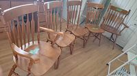 Photo showing two captain chairs with armrests and four regular armless dining chairs arranged in a row on hardwood floor.