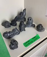 Eight soapstone animal figurines displayed on a white surface, including owl, beaver, seal, and others. Dimensions marked on green tape. Image shows overall lot contents.