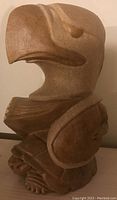 Front view showing stylized eagle head and human face carved in tan stone.