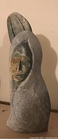 Front view of heavy carved stone sculpture with hooded human face and leaf element behind head